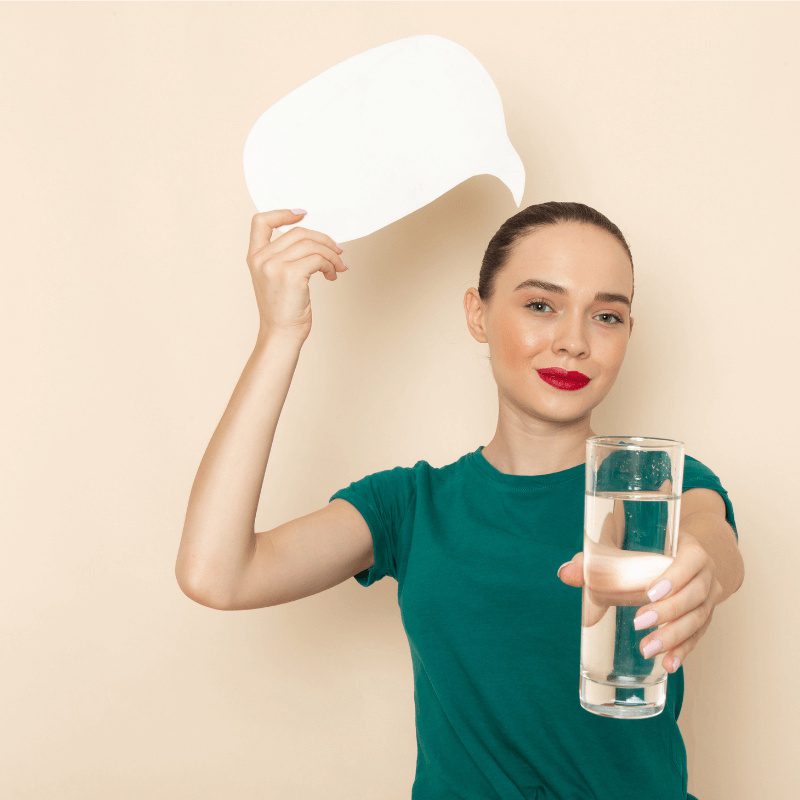 female-dark-green-shirt-blue-jeans-holding-glass-water-white-sign-beige female-dark-green-shirt-blue-jeans-holding-glass-water-white-sign-beige